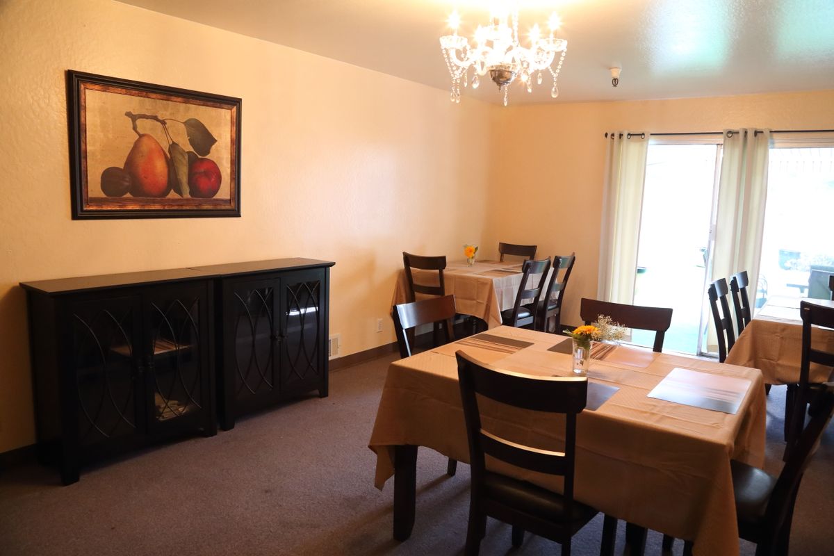 A cozy dining room with two tables, chairs, a chandelier, and a wall painting.