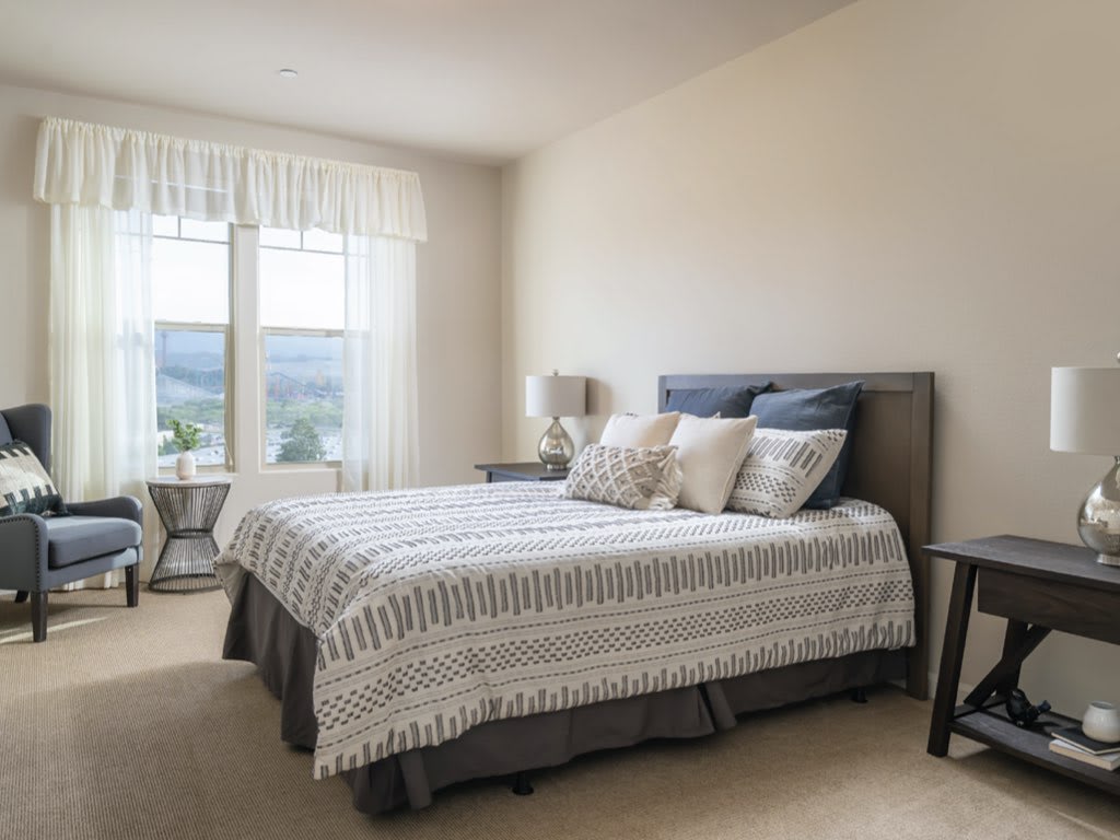 A minimalist bedroom with ample natural light, featuring a neatly made bed and decorative pillows.