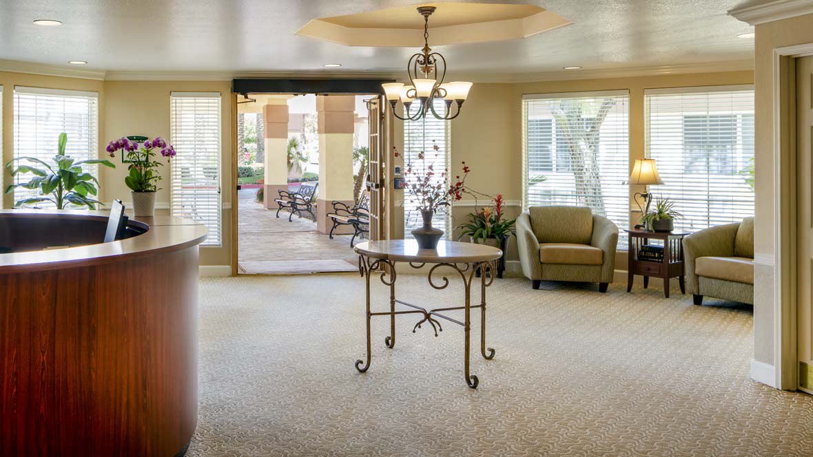A cozy lobby area featuring a central table with a chandelier overhead, armchair seating, and large windows providing natural light.