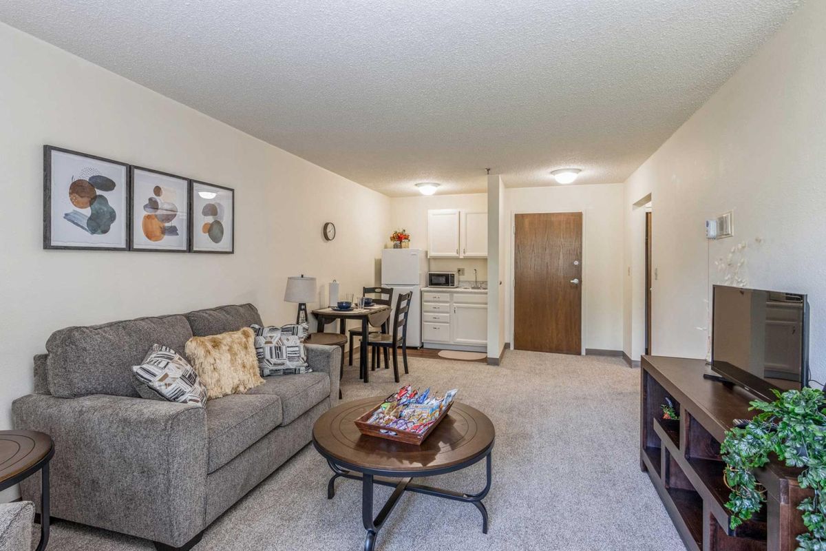 A cozy apartment living room with a sofa, coffee table, and a small dining area adjacent to a kitchenette.