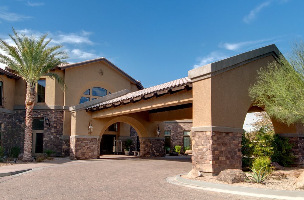 A sunny daytime view of a hotel entrance with palm trees and an archway.