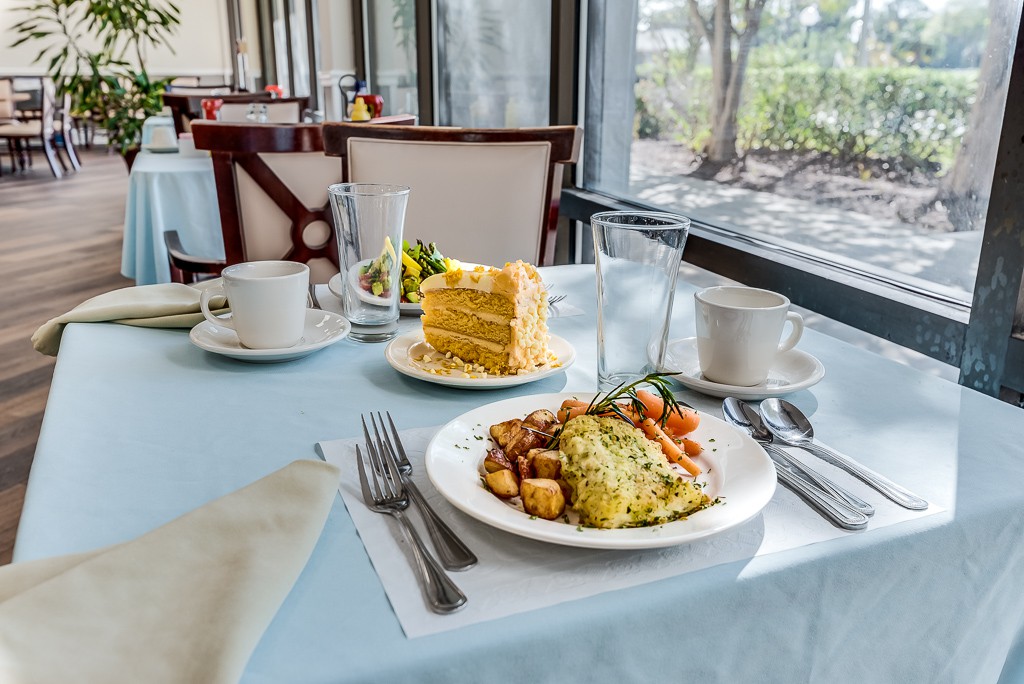 A breakfast table set with an omelette, potatoes, cake, and coffee near a window in a restaurant.
