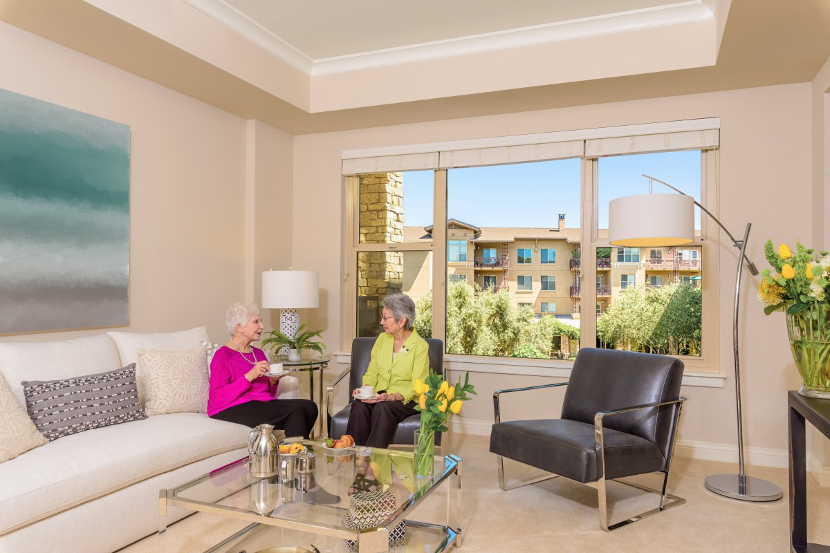 Two people having a conversation in a well-lit living room with modern furnishings.