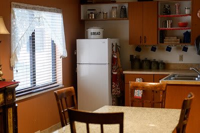 A cozy kitchen interior with a refrigerator, wooden table, and chairs.