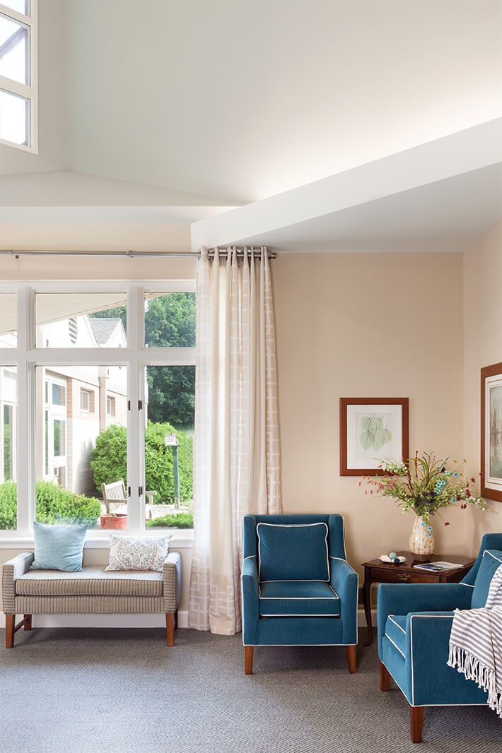 A bright and cozy living room with blue chairs and large windows overlooking a garden.