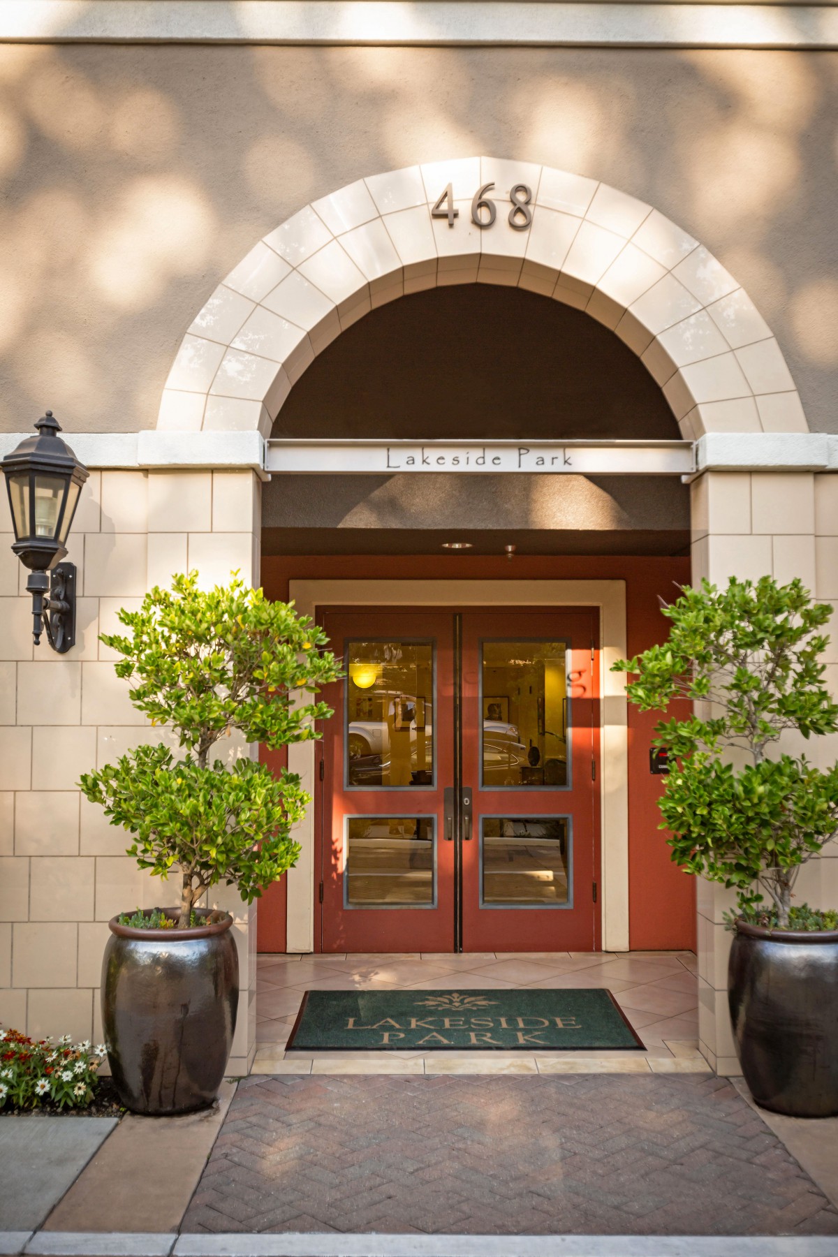 An elegant building entrance with double wooden doors and potted plants.