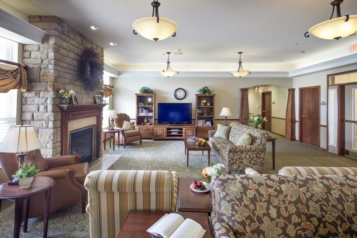 A cozy living room with a fireplace, comfortable sofas, and a television, featuring elegant lighting and well-organized shelves.