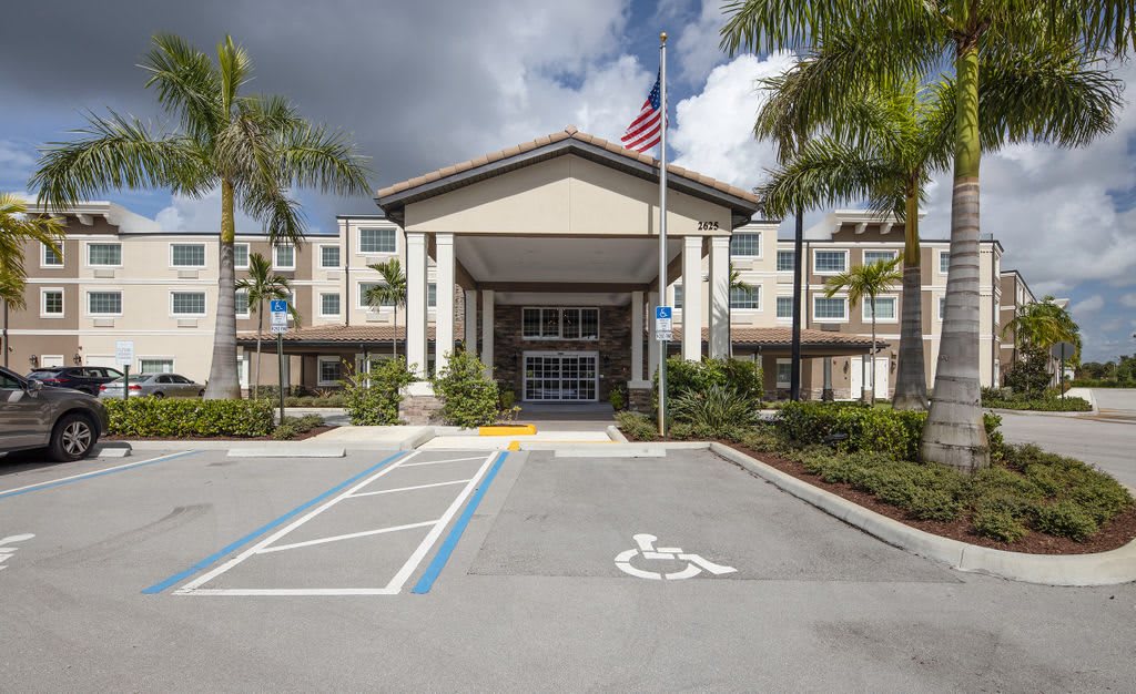 Entrance of a building with palm trees and an American flag, featuring accessibility parking in front.