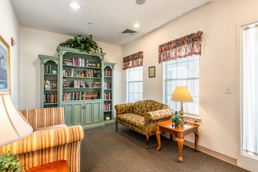 A cozy living room with a bookshelf, couch, and a lamp by the window.