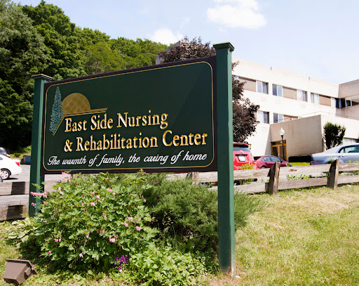 A view of the East Side Nursing & Rehabilitation Center, highlighting its welcoming sign amidst a green landscape.