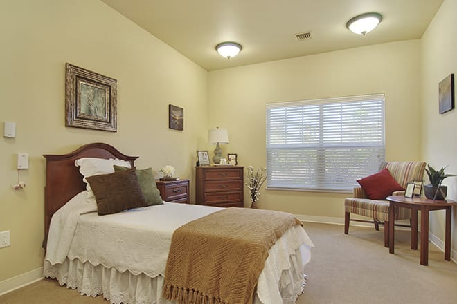 A cozy bedroom with traditional decor featuring a single bed, dresser, and window with blinds.
