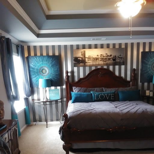 A stylish bedroom featuring striped wallpaper, a wooden bed with decorative pillows, and matching lamps on either side.