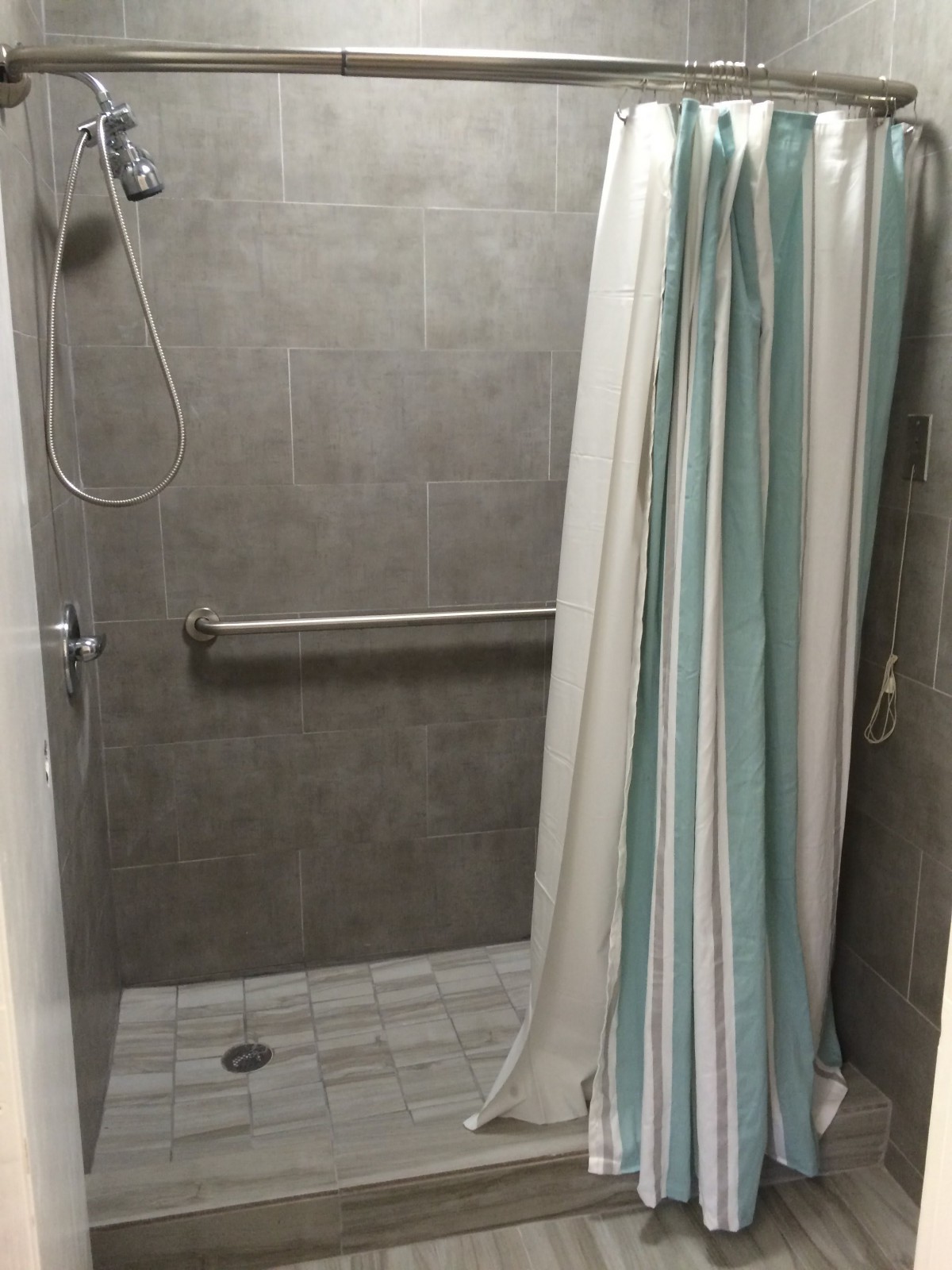 A modern shower area with a striped curtain and gray tiles.