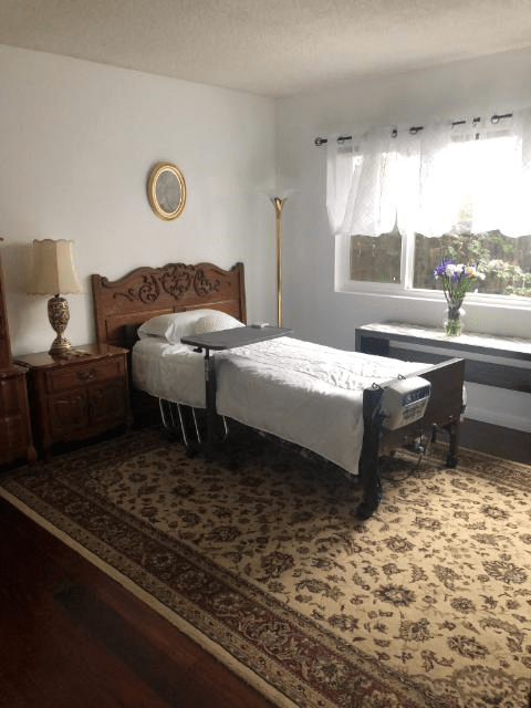A cozy bedroom with a single bed and wooden furniture, featuring a large window and decorative items.