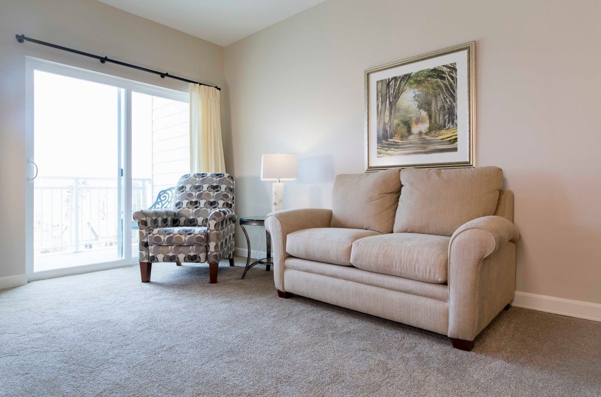 A cozy living room with a beige sofa, patterned armchair, and a large window providing natural light.