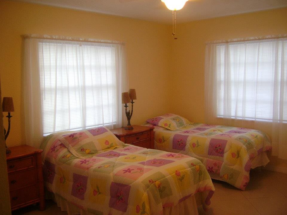 A cozy bedroom with two twin beds adorned with colorful quilts, softly lit by natural light from the windows.