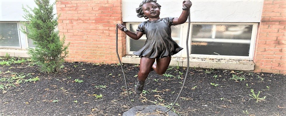 A bronze statue of a child joyfully skipping rope outdoors.