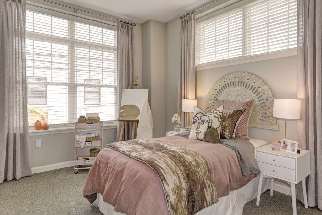 A cozy bedroom with pastel decor and large windows.