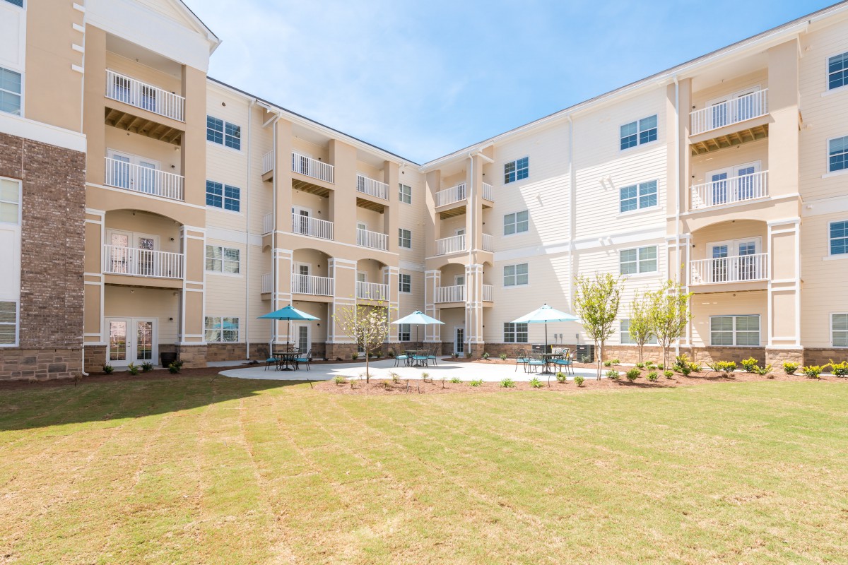 A residential apartment building with balconies and a grassy outdoor area featuring patio umbrellas.