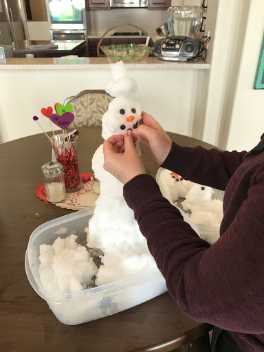A child assembling a fluffy snowman using craft materials.