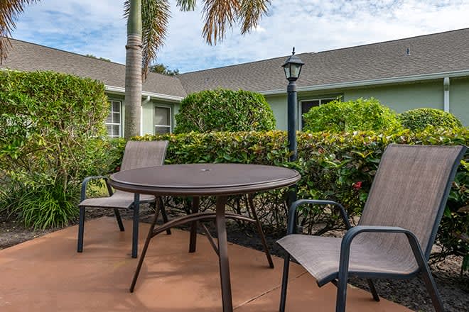 A cozy patio area with a round table and two chairs surrounded by lush greenery.