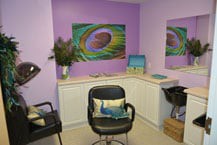 A cozy salon space with purple walls, featuring a comfortable chair and vibrant artwork.