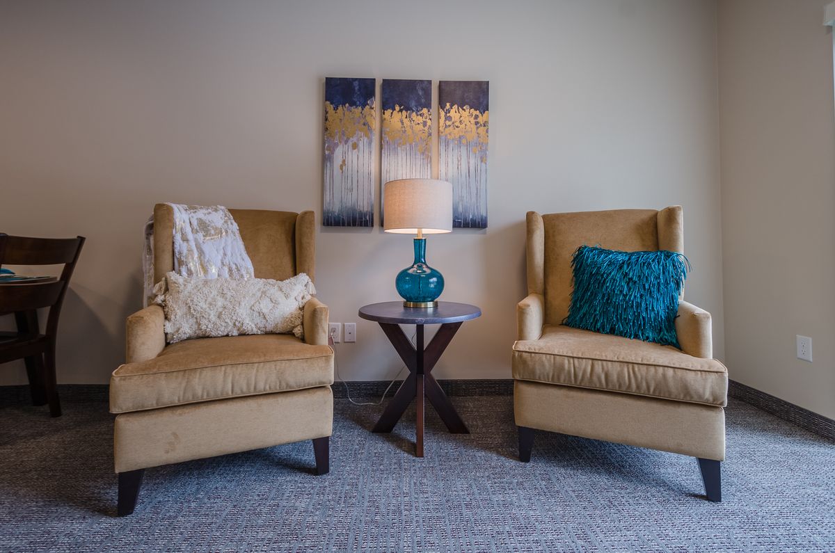 A cozy living room setup with two armchairs, a central lamp on a small table, and artwork on the wall.