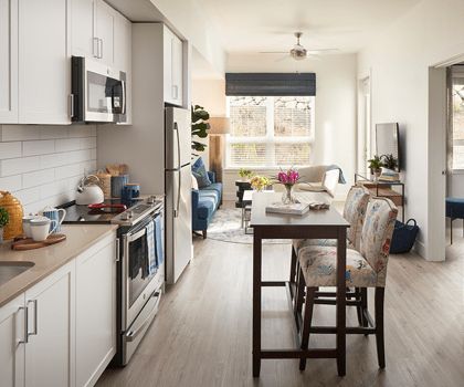 A modern apartment with an open kitchen and dining area, featuring natural light and wood flooring.