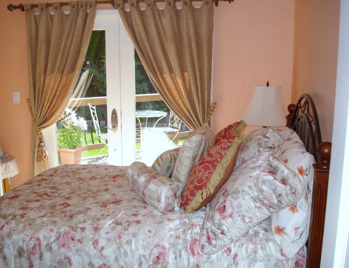 A cozy bedroom interior with floral bedding and draped curtains framing French doors.