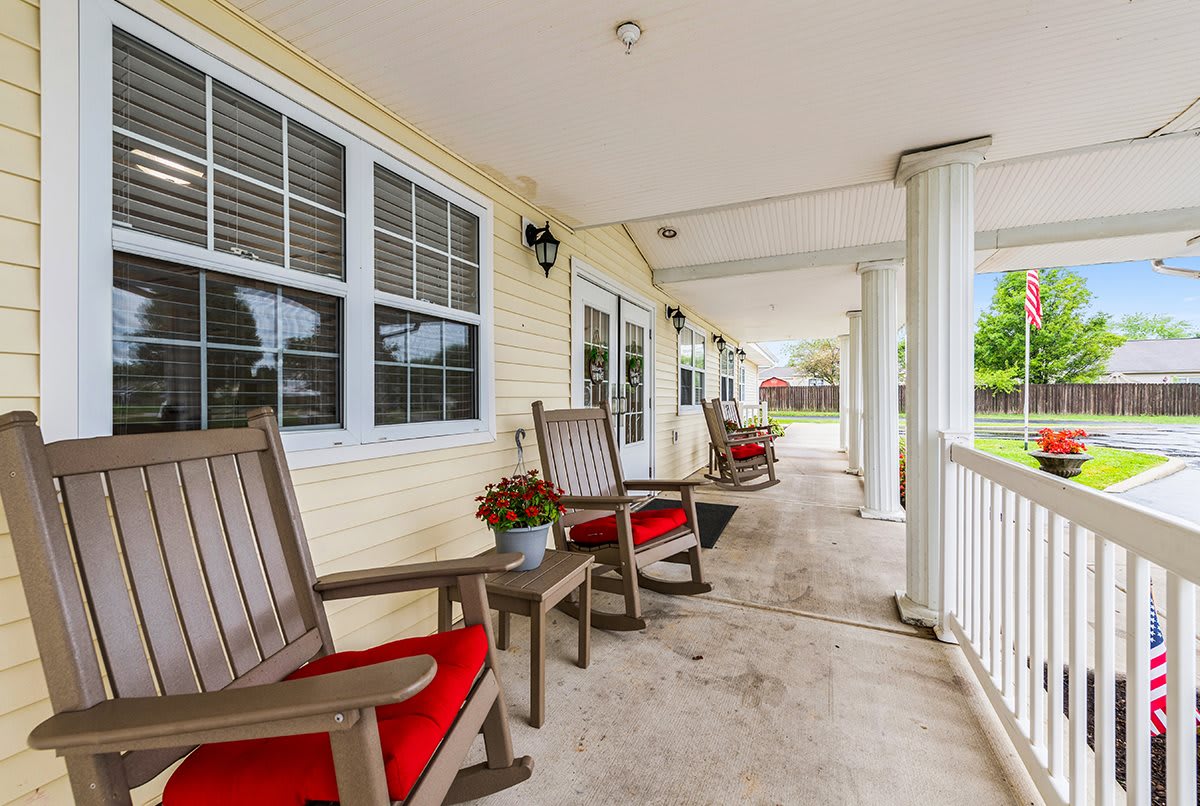 A spacious porch featuring wooden chairs with red cushions and a view of the yard.