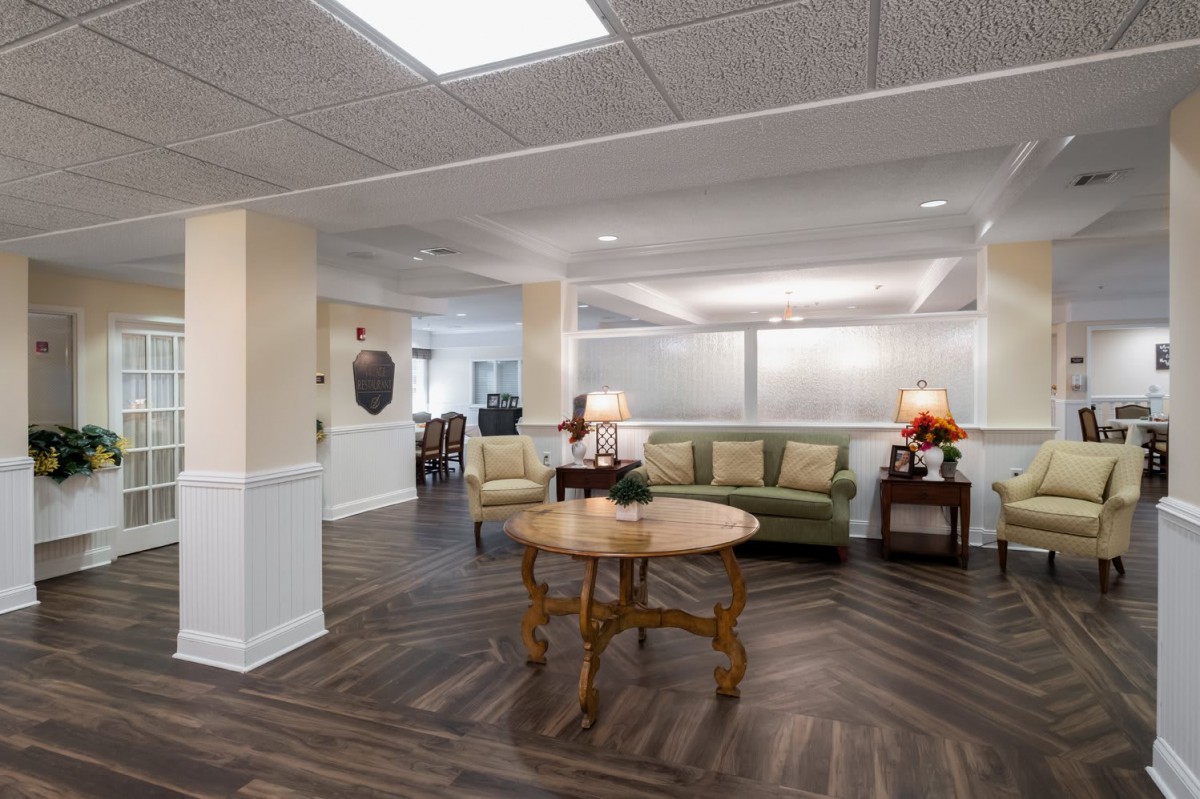 A well-lit lobby area featuring a central wooden table, sofa seating, and decorative elements.