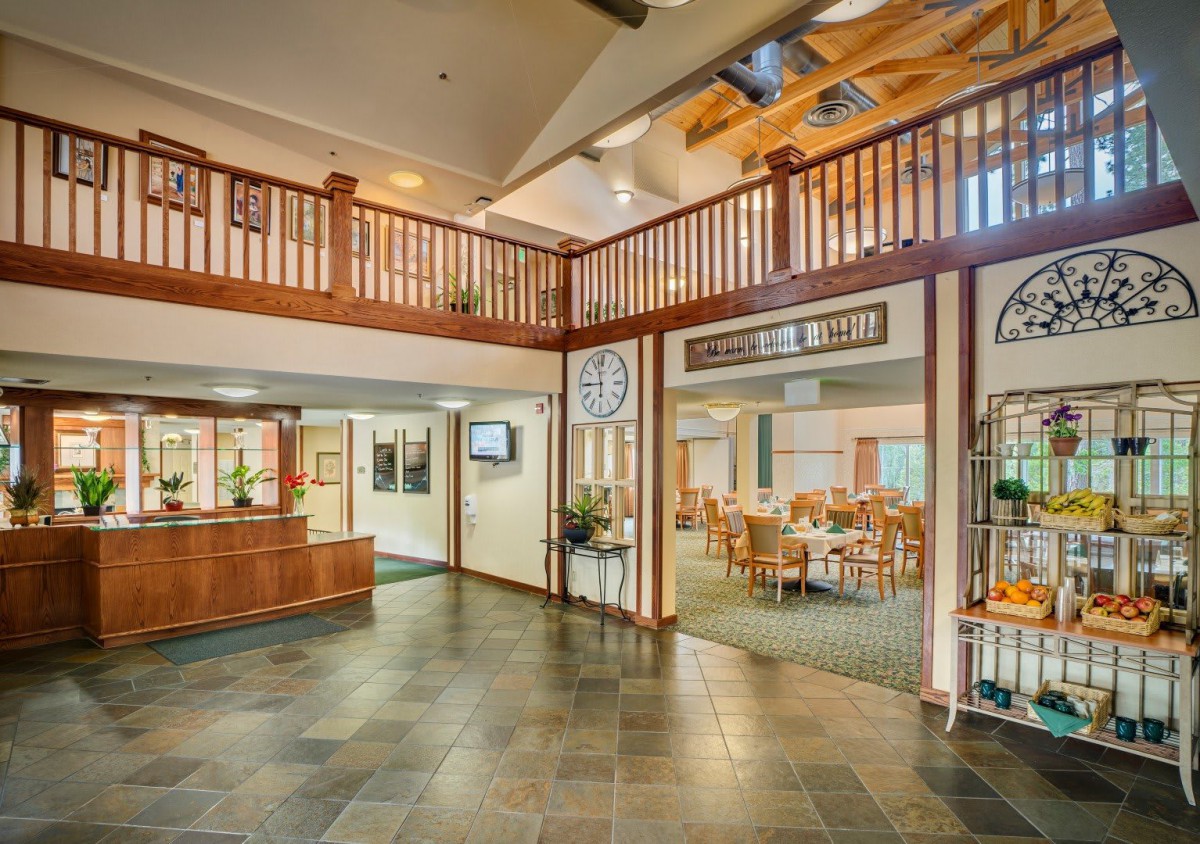 The image shows a spacious lobby with a wooden railing, leading to a dining area.