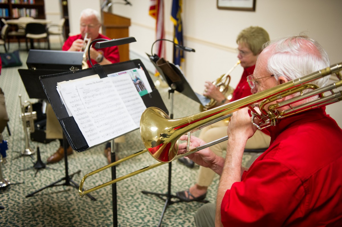 A group of musicians performing with brass instruments indoors, reading from sheet music.