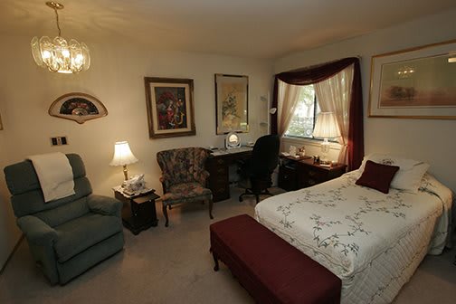 A cozy and traditional bedroom setup with a bed, desk, armchair, and decorative elements.