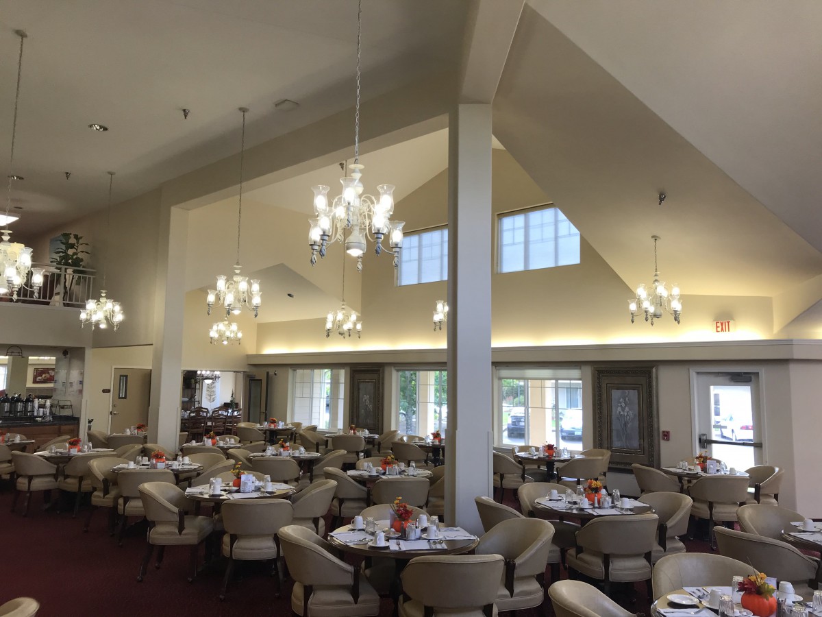 A spacious dining area with elegant chandeliers, round tables, and comfortable seating.