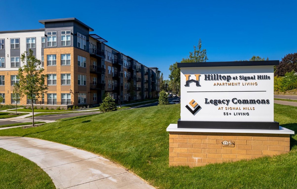 A modern apartment building with a sign reading 'Hilltop on Main Apartments' and 'Legacy Commons'.
