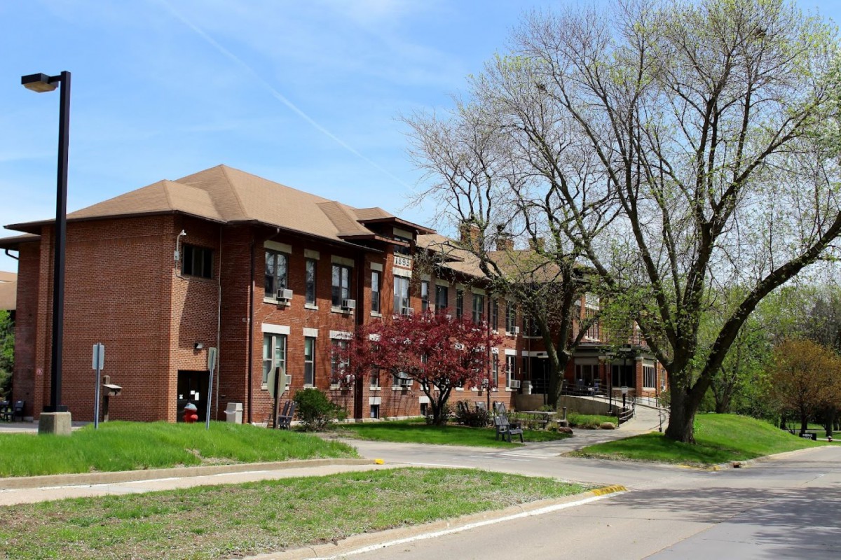 A brick building surrounded by trees and a road on a clear spring day.