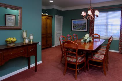 A cozy dining room with green walls, featuring a wooden table and chairs, a chandelier, and decorative elements.