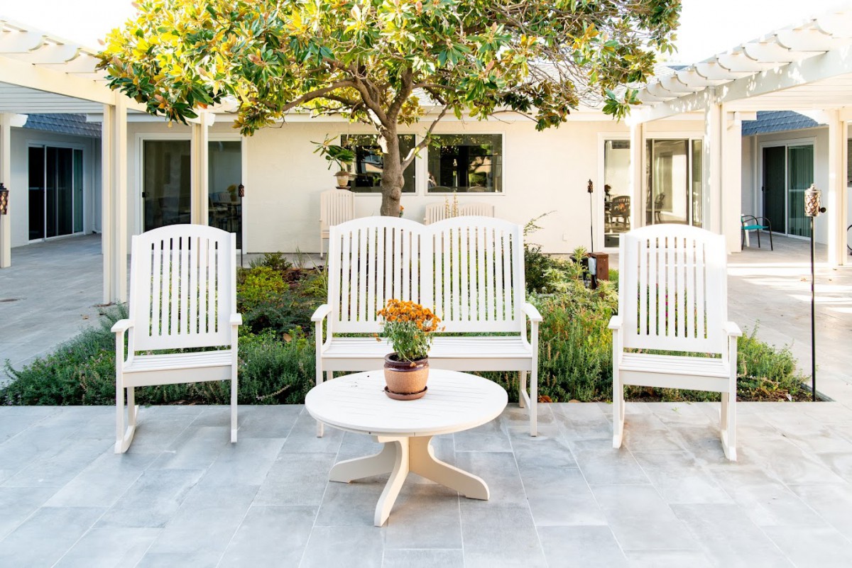 A cozy outdoor patio setup with white chairs and a table, featuring a potted plant centerpiece.