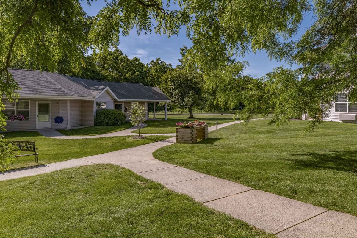 A serene park scene with a pathway, lush grass, and surrounding trees, flanked by residential houses.