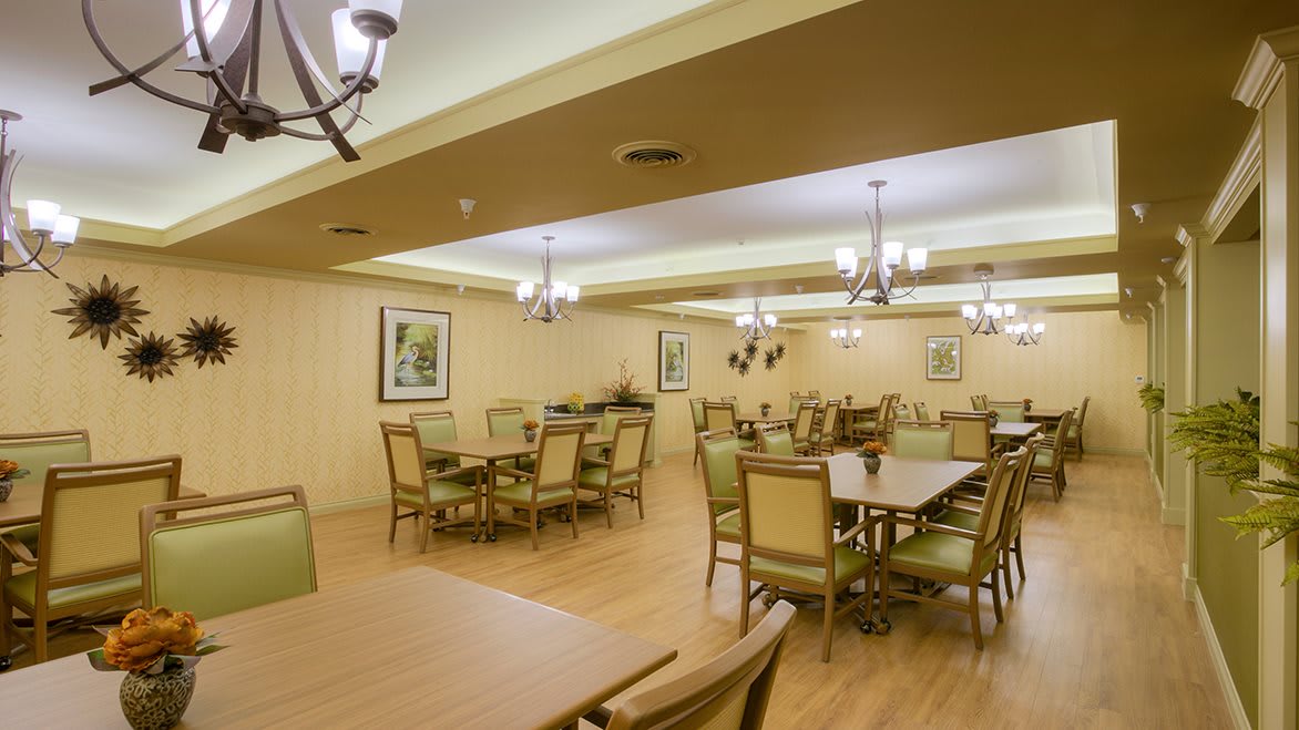 An empty dining room with neatly arranged tables and chairs, featuring elegant chandeliers and a wooden floor.