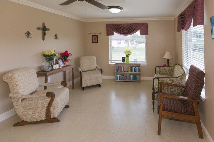 A cozy living room with plush chairs, a window with drapes, and a small bookshelf.