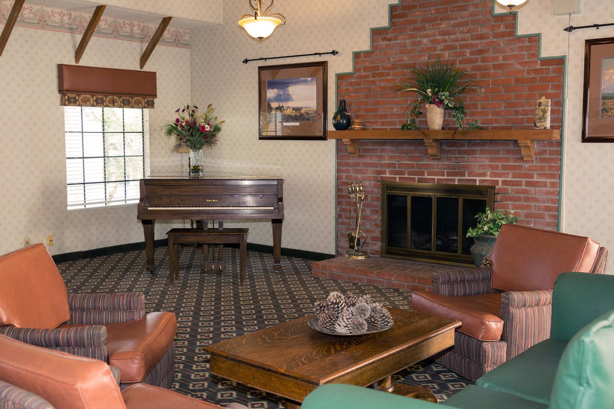 A cozy living room featuring a piano, a brick fireplace, and comfortable furniture.