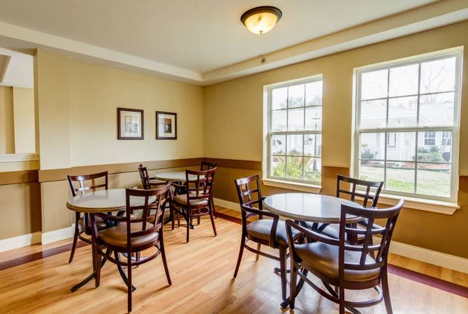 Cozy cafe interior with wooden tables and chairs, brightened by natural light from large windows.