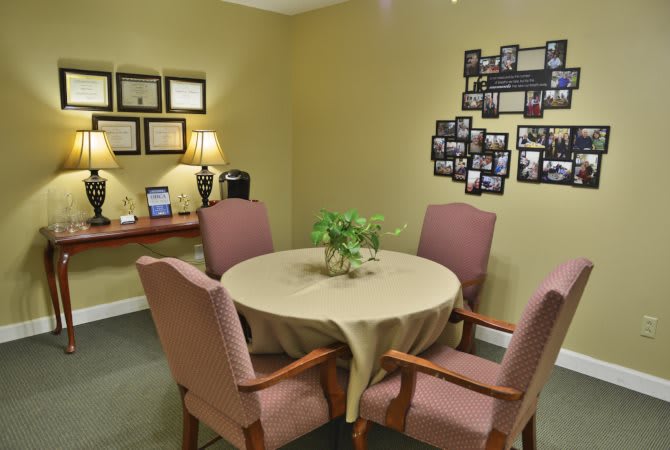 A cozy meeting room with a round table, surrounded by four chairs, and decorated with framed photos on the walls.