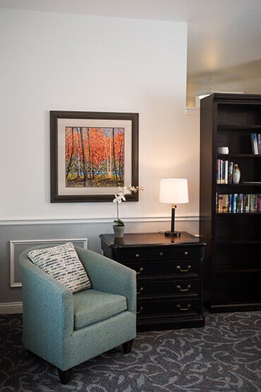 A cozy living room corner featuring an armchair, bookshelf, and framed artwork.