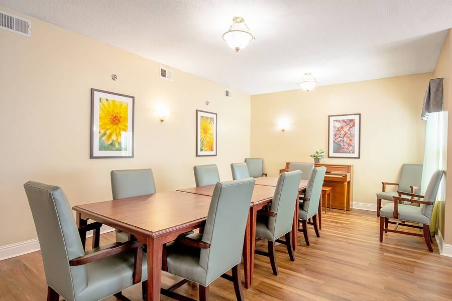 A well-lit dining room with a long wooden table and gray chairs, decorated with floral artwork on the walls.