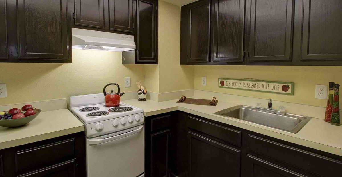 A small kitchen with dark cabinets, a white stove, and a stainless steel sink.