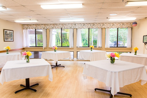 A well-lit event space featuring neatly arranged tables with flower centerpieces, perfect for gatherings and celebrations.