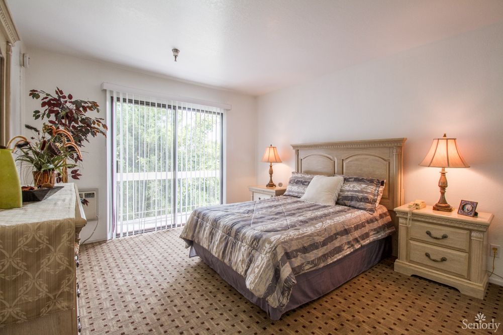 A cozy bedroom with a bed, bedside tables, lamps, and a large window letting in natural light.